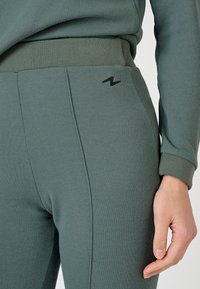 Leggings verdes con relieve y un diseño ajustado, que cuentan con una cintura alta y un pequeño logotipo negro lateral. Textura suave.