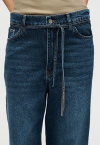 Σκούρο μπλε τζιν με άνετη εφαρμογή, με ελαστική μέση, μπροστινές τσέπες και λεπτομέρεια κλεισίματος με κορδόνι.