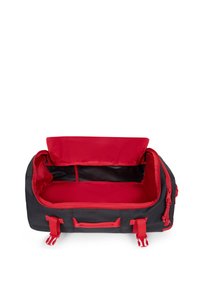 Czarna torba sportowa z czerwoną podszewką, z dwoma górnymi uchwytami, zamknięciem na zamek i bocznymi klamrami. Wnętrze ma jedną dużą komorę.