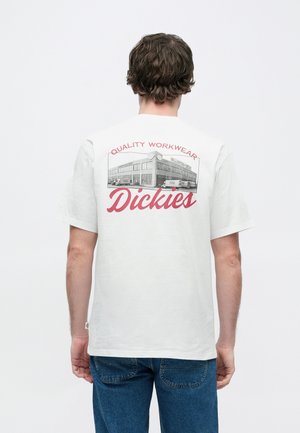 Tricou din bumbac alb, cu grafică a unei clădiri și textul "QUALITY WORKWEAR Dickies" în roșu, croială lejeră, mâneci scurte.