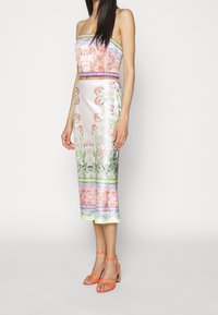 Ensemble deux pièces à motif floral avec une finition satinée ; le haut dispose de fines bretelles et d'une silhouette ajustée, tandis que la jupe est mi-longue et droite.