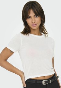 Maglietta bianca a maniche corte con scollatura rotonda, tessuto leggero e vestibilità leggermente cropped. Abbinata a pantaloni neri a vita alta e cintura.