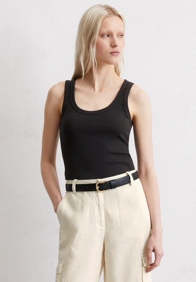 Schwarzes, enges Tanktop mit rundem Ausschnitt, kombiniert mit hellbeigen Leinenhosen und einem schwarzen Gürtel mit goldener Schnalle.