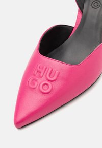 Gros plan d’une chaussure à bout pointu rose vif avec intérieur noir et logo embossé "HUGO" sur la surface supérieure avant.