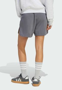 Pantaloni corti grigi dal taglio morbido, con spacchi laterali e una texture morbida. Abbinati a scarpe grigie con accenti argentati e calze grigie con righe bianche.