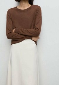 Haut marron à manches longues avec un col rond, fabriqué dans un matériau doux, associé à une jupe fluide de longueur moyenne de couleur crème.