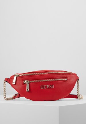 Rode leren Guess heuptas met twee gouden ritsen, kettingschouderband en merklogo centraal op de voorzak.