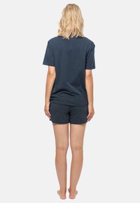 Marineblauw t-shirt met korte mouwen, gecombineerd met marineblauwe shorts met witte stippen, weergegeven van achteren.