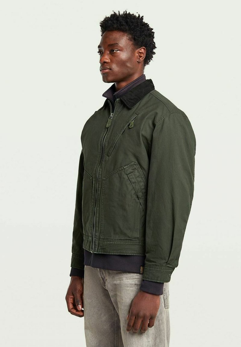 Veste bomber verte avec fermeture éclair à l'avant, col montant et tissu texturé. Comprend des poches avant et des poignets côtelés. Design minimaliste.