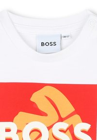 T-shirt bianca BOSS con colletto a giro, caratterizzata da una grande grafica rossa e gialla e scritte in bianco in grassetto. Tessuto di cotone morbido.