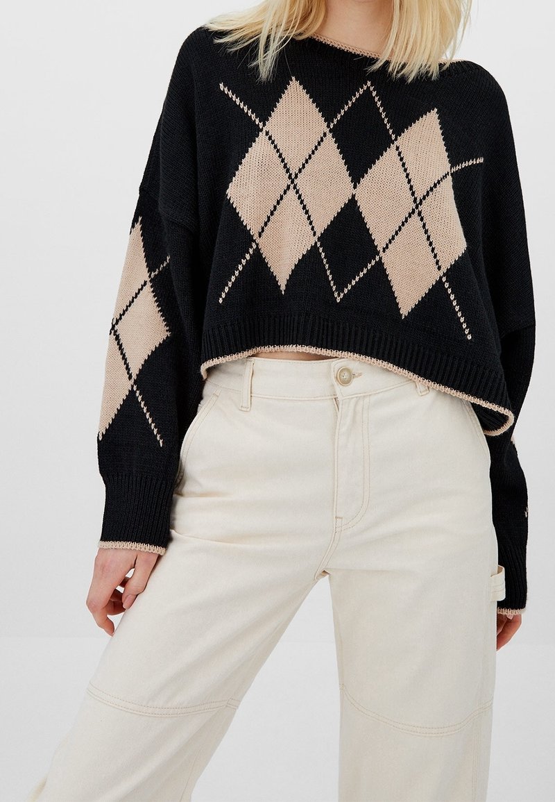Pull court noir avec motif argyle beige associé à un pantalon taille haute écru, montré des épaules jusqu'à mi-cuisse.