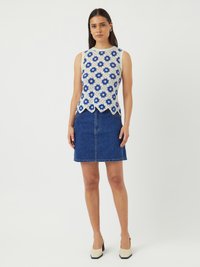Blonde bluse med blå blomster mønster og bølget kant, kombinert med en tettsittende jeanskjørt. Modellen har på seg beige blokk hæler.