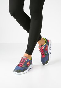Chaussures de sport avec une tige en mesh bleu marine et gris, des accents rose néon et des semelles en caoutchouc blanches. Dotées de lacets lumineux et d'une semelle coussinée.