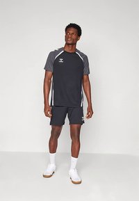 T-shirt desportiva preta com detalhes cinzentos, mangas curtas e riscas brancas. Combinada com calções combinando e ténis brancos.