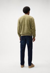 Maglione in pile verde oliva con una superficie testurizzata, abbinato a pantaloni cargo blu scuro con diversi taschini e una vestibilità rilassata.