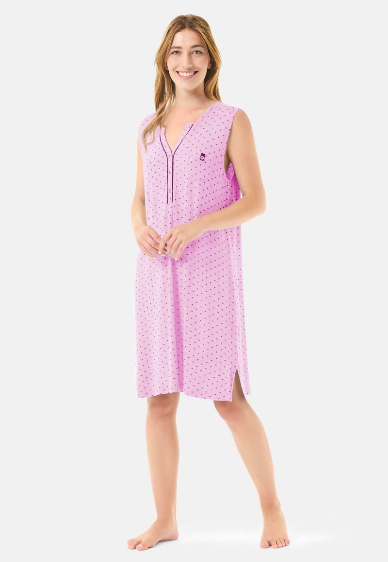 Camisón sin mangas en rosa claro con pequeños lunares negros, con un escote en V abotonado y aberturas laterales para facilitar el movimiento.