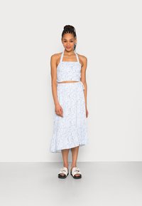Conjunto de dois peças em azul claro com padrão floral, apresentando um top halter cropped e uma saia midi fluida com bainha frisada. Combinado com sandálias brancas de deslizar.