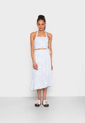 Conjunto de dois peças em azul claro com padrão floral, apresentando um top halter cropped e uma saia midi fluida com bainha frisada. Combinado com sandálias brancas de deslizar.