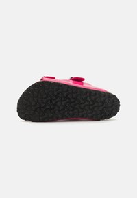 Scarpa di gomma rosa con suola nera testurizzata, dotata di due cinture regolabili sulla parte superiore, progettata per comfort e durata.