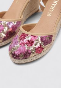 Zapatos de cuña espadrille en rosa y dorado con upper de tela beige y suela de yute trenzado. Diseño de flor de lentejuelas en la parte delantera.