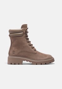 Braune Wildleder-Stiefeletten mit gepolstertem Kragen, runden Schnürsenkeln und einer groben Gummisohle mit strukturiertem Muster. Prägierte Logo an der Seite.