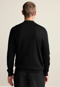 Čierny pletený sveter s klasickým strihom, okrúhlym výstrihom a dlhými rukávmi. Má rebrované manžety a lem pre lepšiu štruktúru.