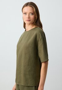 Top in lino verde oliva con scollatura rotonda e maniche corte, caratterizzato da una vestibilità comoda e una superficie liscia e declinata.