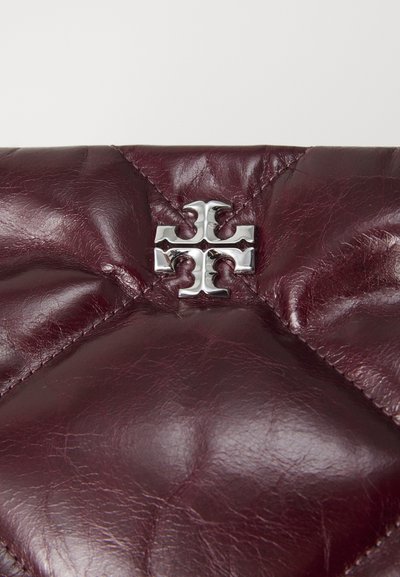 Burgundijas ādas clutch ar šuvju pārklājuma tekstūru un sudraba logotipa emblēmu vidū. Kompakta un taisnstūrveida forma.