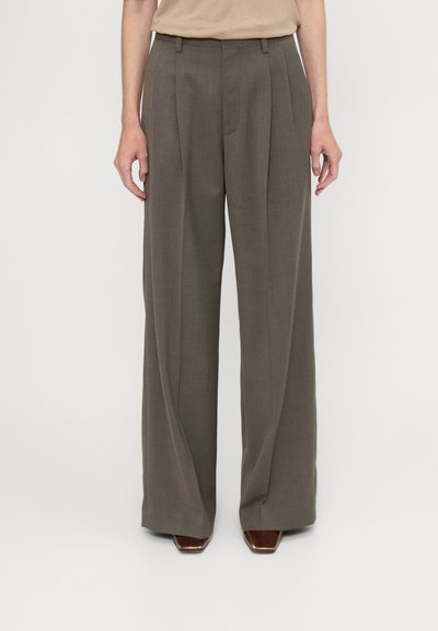 Wide-leg trousers in dark brown fabric, featuring a textured finish, front pleats, and a high waistband. Paired with pointed heels.