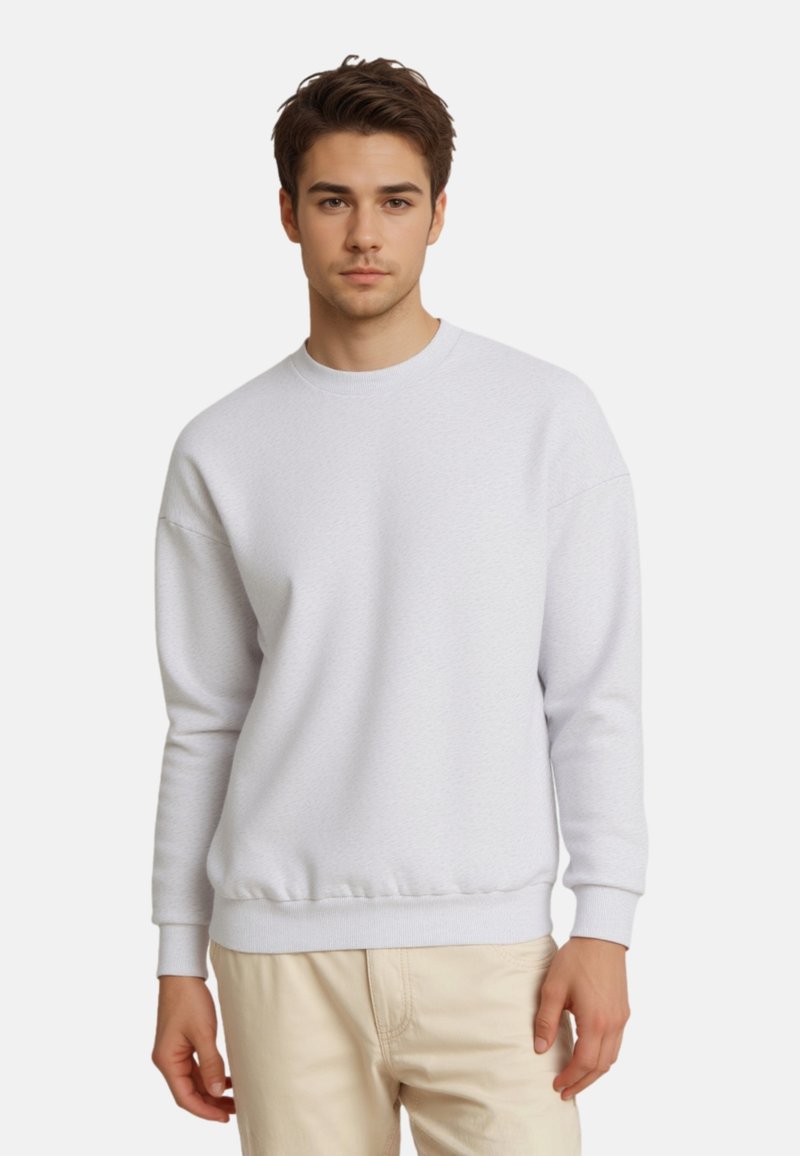 Sweatshirt gris clair avec un col rond, des manches longues, des poignets et un ourlet côtelés, et une surface légèrement texturée. Porté sur un pantalon beige.