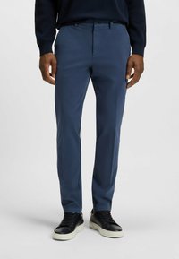 Granatowe spodnie o slim fit, wykonane z gładkiego materiału. Posiadają dwie przednie kieszenie oraz zapięcie na guzik. Noszone z czarnymi trampkami.