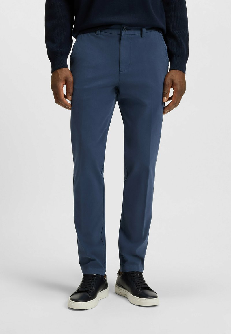 Granatowe spodnie o slim fit, wykonane z gładkiego materiału. Posiadają dwie przednie kieszenie oraz zapięcie na guzik. Noszone z czarnymi trampkami.