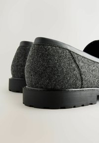 Grijze instapschoenen van soepel materiaal met een zwarte rubberen zool en glanzende leren accenten. Ronde vorm en gestructureerd oppervlak op het bovenste deel.