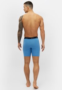 Herrars blå boxerkalsonger med svart midjeband, tillverkade av mjukt bomullstyg, i medellång längd som når till mitten av låret och med en åtsittande design.