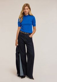 Top tricotat de un albastru strălucitor, cu mâneci scurte, asortat cu pantaloni evazați din denim închis, cu buline albe. Accent cu o curea neagră și pantofi cu toc.