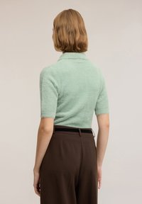 Mintgrön, fluffig tröja med korta ärmar, utrustad med en ribbad krage och en kortare design, kombinerad med bruna byxor med hög midja.