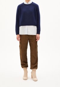 Marineblauwe cropped trui, witte blouse eronder, bruine cargobroek met zakken, beige getextureerde schoenen met hak. Eenvoudig, modern ontwerp.