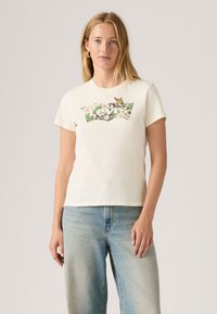 Ένα off-white βαμβακερό μπλουζάκι διαθέτει λογότυπο Levi's με floral σχέδιο, στρογγυλή λαιμόκοψη, κοντά μανίκια και άνετη εφαρμογή. Φοριέται με ανοιχτόχρωμο μπλε τζιν.