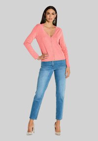 Roze cardigan met een V-hals en knoopsluiting, gecombineerd met blauwe tapered jeans en gepatternde hoge hakken. Gladde textuur, casual pasvorm.