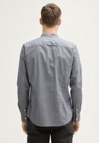 Camicetta grigia a maniche lunghe con colletto button-down, realizzata in un tessuto leggermente testurizzato e con orlo curvo. Dettagli con bottoni sulle maniche.
