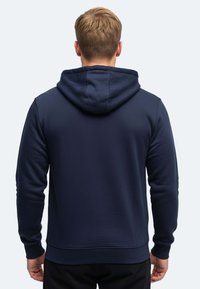 Felpa blu navy con cappuccio regolabile, polsini e orlo a costine. Texture liscia, design aderente e stile minimalista.