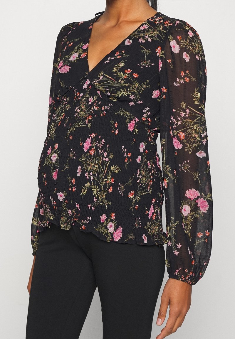 Blusa nera con motivo floreale, caratterizzata da un profondo scollo a V e maniche lunghe a palloncino. Realizzata in tessuto leggero e testurizzato con dettagli di orlo arruffato.