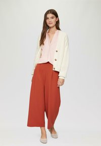 Gehaakte creme cardigan met grote knopen, gecombineerd met een lichtroze blouse en rustkleurige broek met wijde pijpen. Eenvoudige, gestructureerde stof overal.