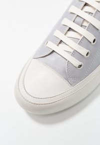 Šedé kožené tenisky s texturovaným svrškem, hladkým zaobleným špičkou, smetanovými tkaničkami a kontrastní bílou gumovou podrážkou.