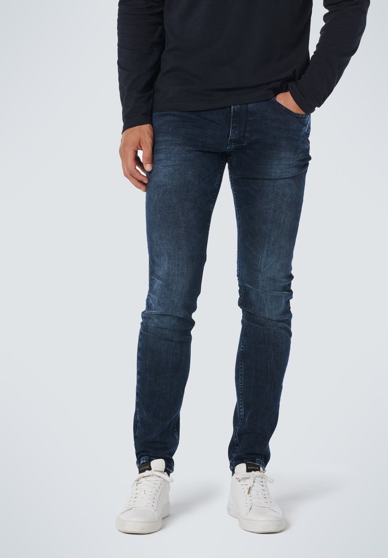 Donkerblauwe, slim-fit jeans van denim, met een klassieke vijf-pocket ontwerp en subtiele vervaging, gecombineerd met witte sneakers.