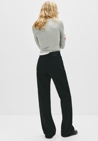 Pantalon noir à jambes larges en denim, avec des poches arrière et une texture lisse. Un haut gris à manches longues est porté en dessous.