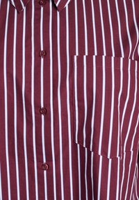 Bordo krekls ar vertikālām baltām un gaiši ziliem svītrām, priekšējais kabatiņš labajā pusē un bordo pogas pa vidu.