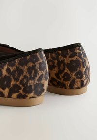Baletní boty s leopardím vzorem, s texturovaným svrškem, flexibilním černým olemováním a světlohnědou gumovou podrážkou. Zaoblený design v zadní části.
