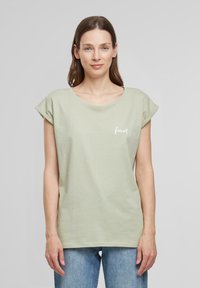 T-shirt vert clair à manches courtes en coton doux, avec un col rond et un petit texte blanc "forever" sur la poitrine gauche.