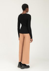 Schwarzes, geripptes Langarmoberteil mit einem tiefen Rückenausschnitt und goldenen Akzenten, kombiniert mit pfirsichfarbenen, weiten Hosen und schwarzen Plateauschuhen.